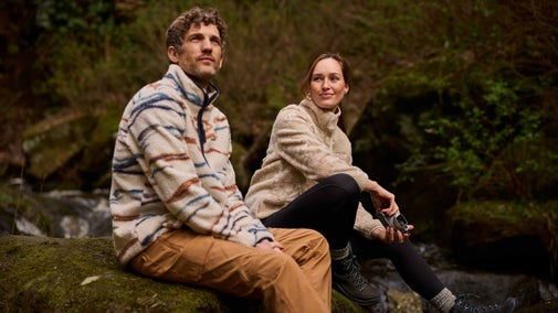 A couple sit on a boulder next to a river